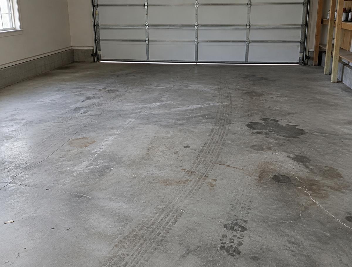 Bare gray garage concrete with oil stains, tire marks and hairline cracks before coating